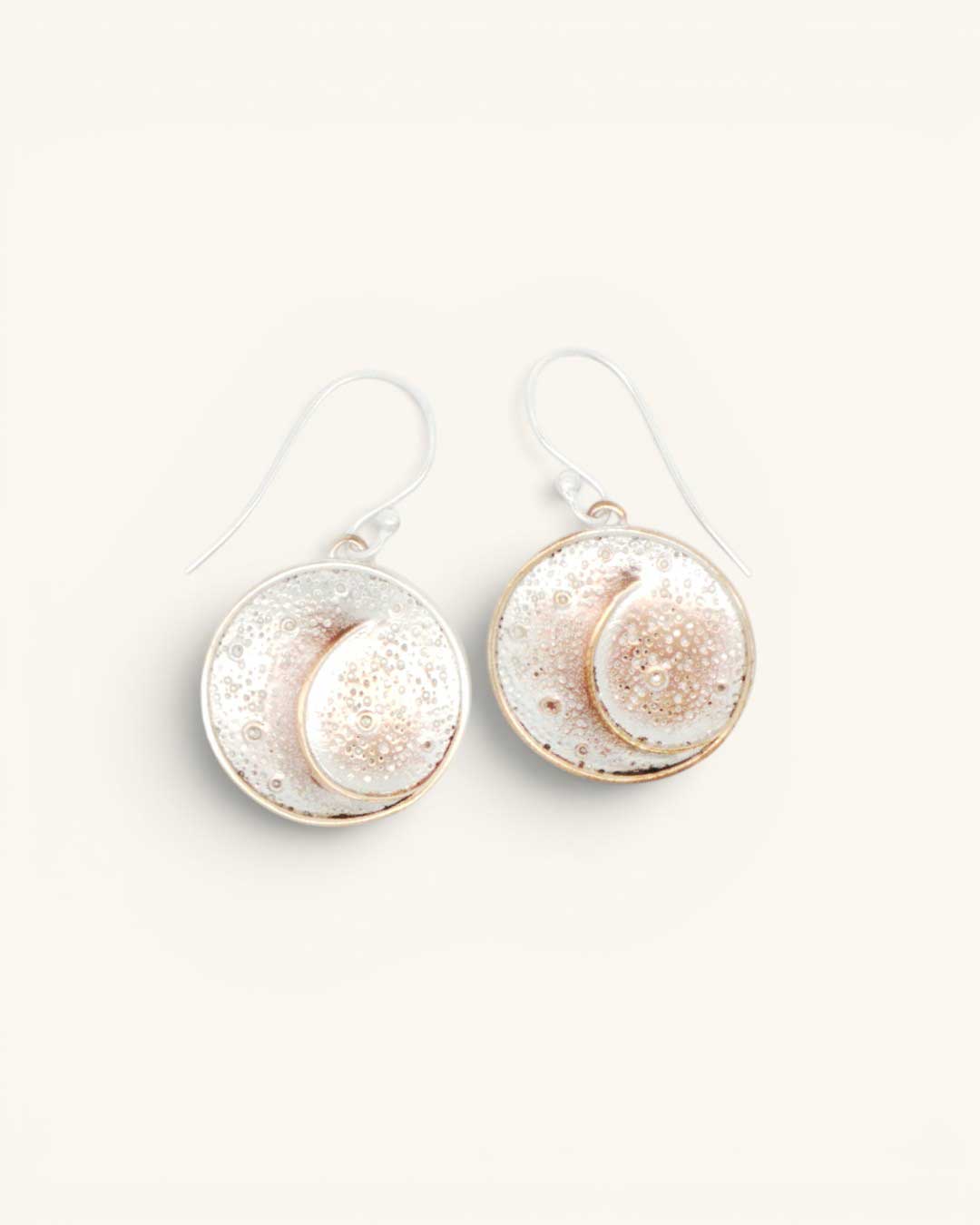 Crescent moon disc earrings viewed from above on a light background, showing the curved crescent relief and dotted bronze disc surface