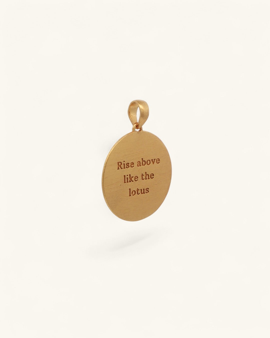 Back of gold plated brass lotus pendant at an angle showing engraved text reading Rise above like the lotus