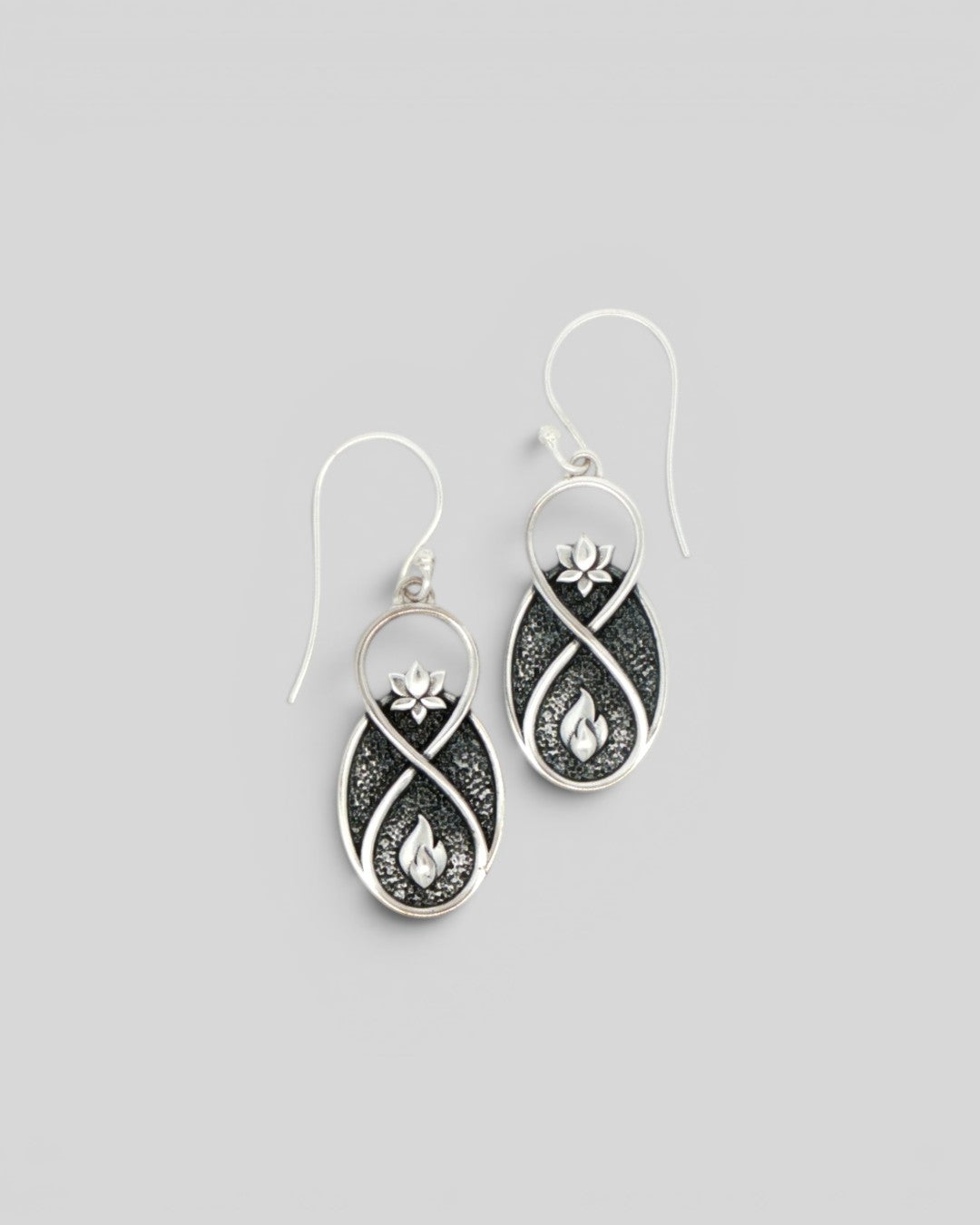 Pair of Lotus Infinity Flame silver drop earrings at a slight angle, showing lotus and flame motifs on oxidized background