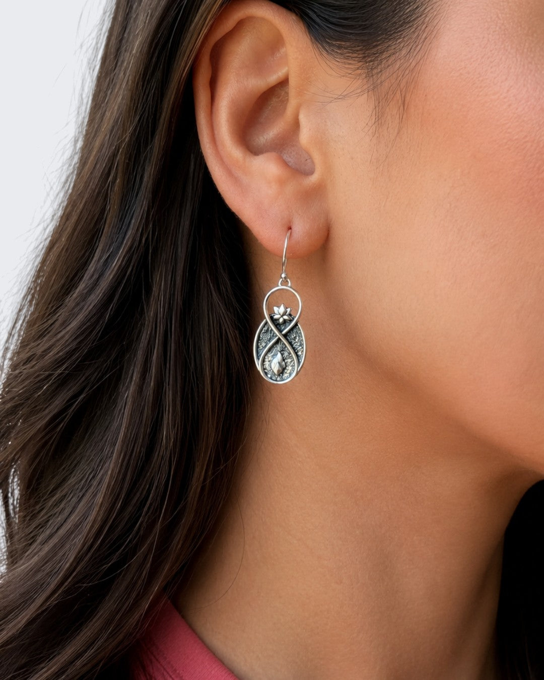 Lotus Infinity Flame drop earring worn on model's ear, showing infinity-shaped silver pendant with lotus top detail