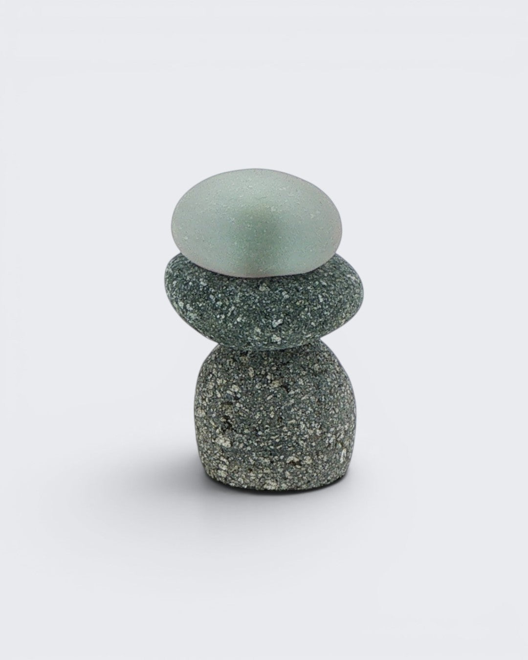 Single small mini stacked stone cairn with a frosted sea glass top piece over two grey speckled stones, front detail view