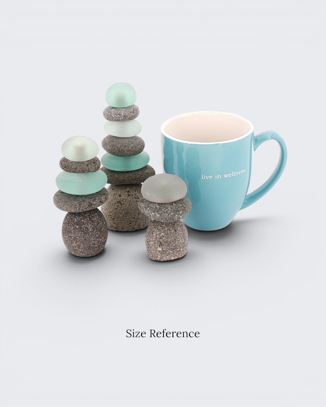 Two mini stacked stone cairns with sea glass placed next to a standard coffee mug to illustrate relative size scale