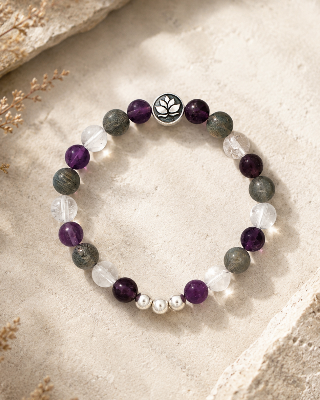 Amethyst, labradorite, and clear quartz lotus bracelet styled on a stone surface with dried botanicals in background