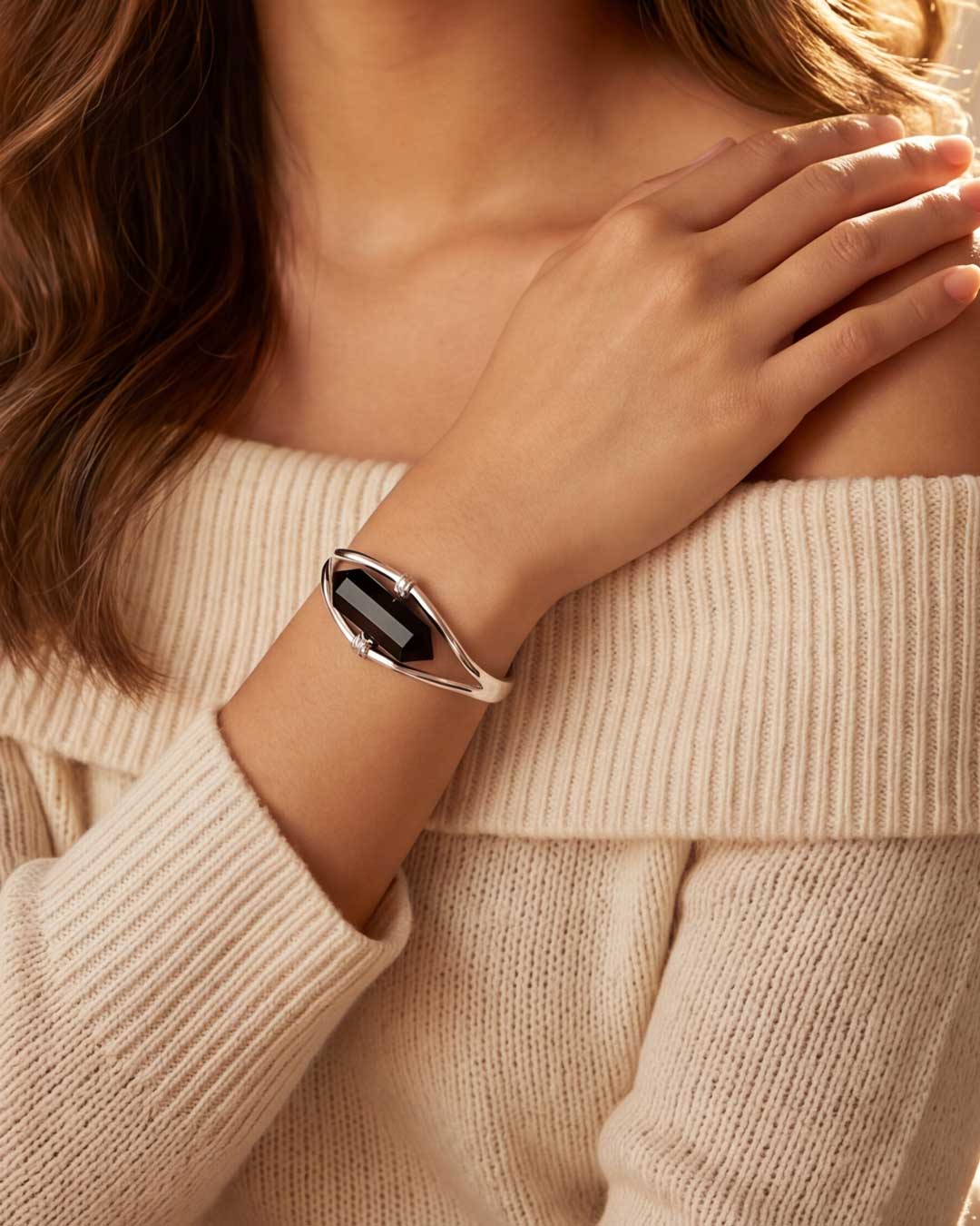 Woman wearing silver black onyx point cuff bracelet on wrist with off-shoulder cream sweater