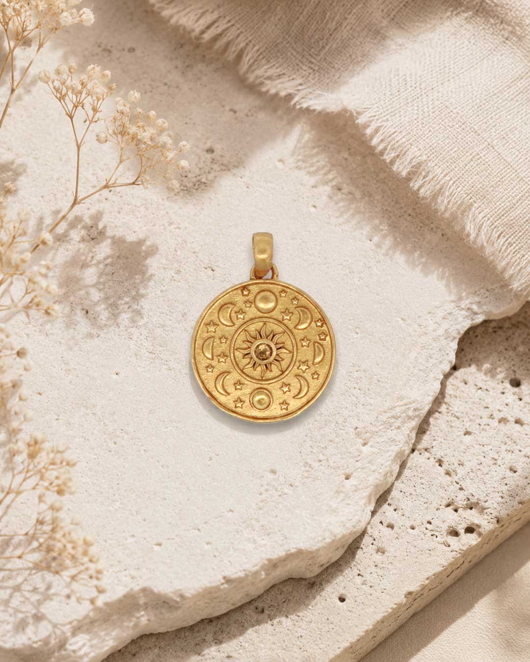 Celestial Sun and Moon Citrine Pendant in gold-plated brass styled flat on a stone surface with dried flowers and linen