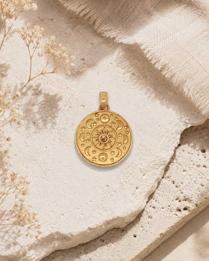 Celestial Sun and Moon Citrine Pendant in gold-plated brass styled flat on a stone surface with dried flowers and linen