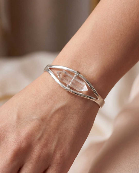 Clear quartz crystal point cuff bracelet worn on a woman's wrist, silver cuff with central gemstone visible
