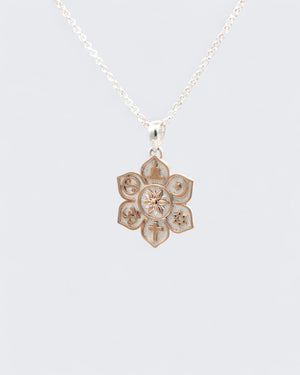 Coexist Harmony Lotus Pendant hanging on a silver rolo chain against a gray background, front face with religious symbols visible