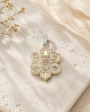 Coexist Harmony Lotus Pendant resting on a textured stone surface beside dried flowers, front face showing rose-gold unity symbols