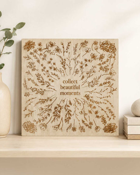 Collect Beautiful Moments engraved wood wall sign leaning on a shelf beside a ceramic vase and stacked books
