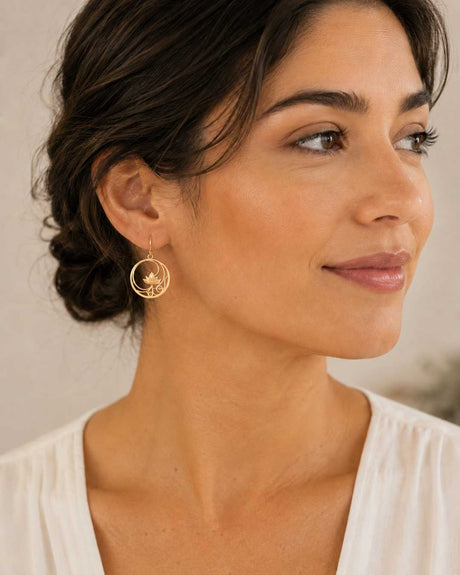 Woman wearing gold plated openwork lotus circle drop earring on ear, side profile close-up view