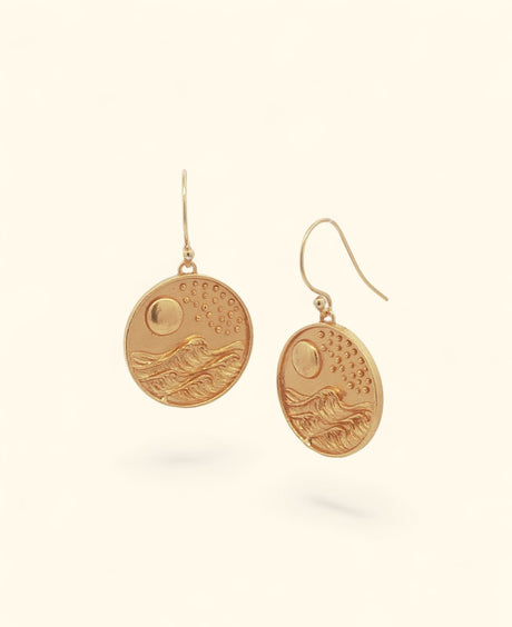 Gold-plated brass coin drop earrings with embossed moon, stars, and ocean waves, front view showing both earrings floating