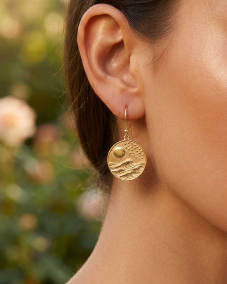 Gold-plated brass moon and wave coin drop earring worn on model's ear, close-up showing scale and embossed disc detail