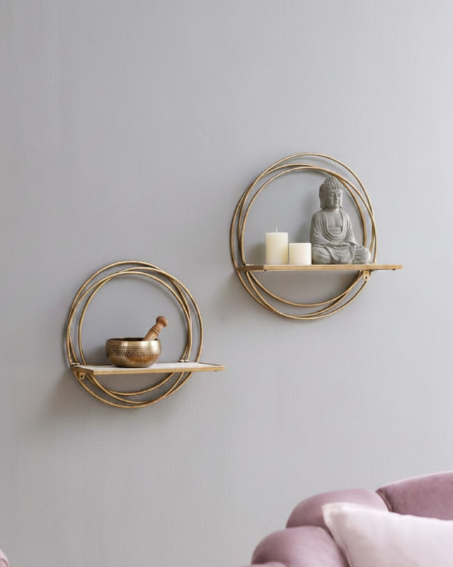 Two golden ring floating wall shelves on grey wall, lower shelf with singing bowl, upper with pillar candles and Buddha statue