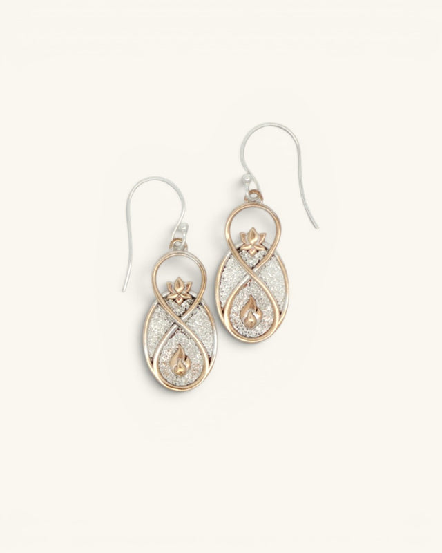 Infinite Lotus drop earrings front view, gold-tone infinity frame with lotus and flame motifs over glitter silver background