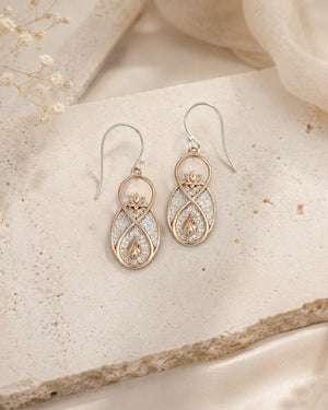 Infinite Lotus drop earrings laid on a textured stone surface beside dried flowers and cream fabric, pair view