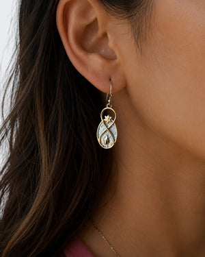 Infinite Lotus earring worn on model's ear, showing infinity-shaped bronze drop with lotus top and flame detail