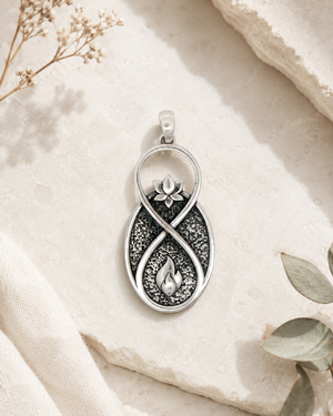 Infinite Lotus Flame Pendant silver charm styled flat on stone surface with dried botanicals and eucalyptus leaves in the background