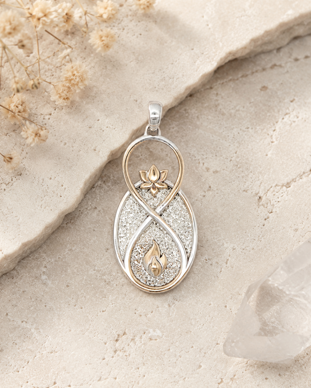 Infinite Lotus & Flame Pendant resting on rough stone surface with dried flowers and crystal point in background