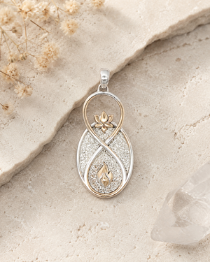 Infinite Lotus & Flame Pendant resting on rough stone surface with dried flowers and crystal point in background