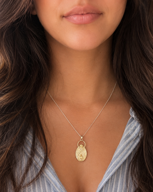 Infinite Lotus & Flame Pendant worn on silver chain at a woman's neckline over an open-collar blue striped shirt