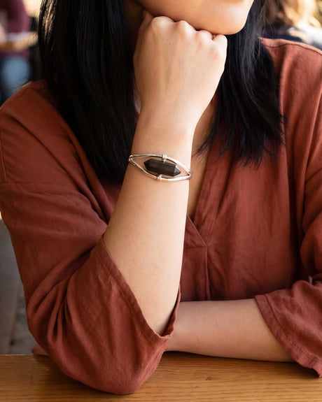 Woman in rust-colored blouse wearing silver labradorite point cuff bracelet, resting chin on hand