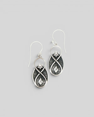Pair of Lotus Infinity Flame silver drop earrings at a slight angle, showing lotus and flame motifs on oxidized background
