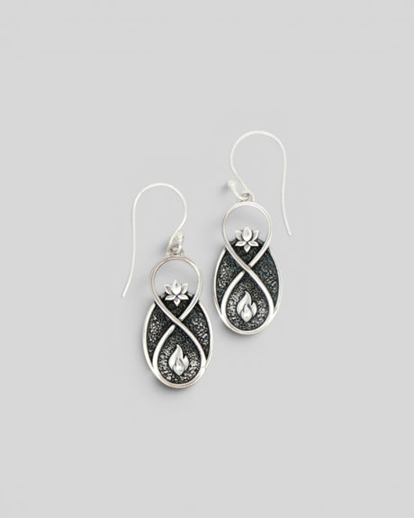 Pair of Lotus Infinity Flame silver drop earrings at a slight angle, showing lotus and flame motifs on oxidized background