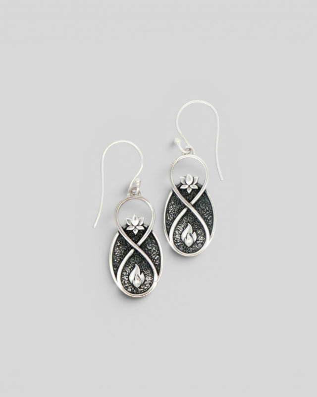 Pair of Lotus Infinity Flame silver drop earrings at a slight angle, showing lotus and flame motifs on oxidized background