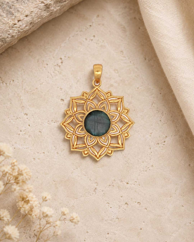 Styled flat-lay of gold lotus mandala pendant with labradorite center stone on travertine surface with dried flowers