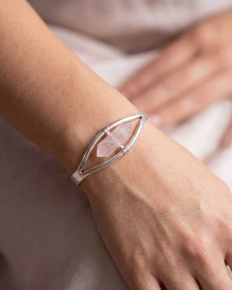 Woman wearing silver rose quartz point cuff bracelet on wrist with soft blush fabric background