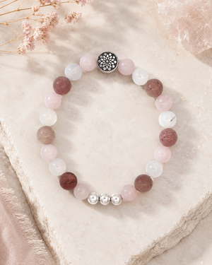 Mandala gemstone stretch bracelet laid on a stone surface with dried pink florals and blush fabric in the background