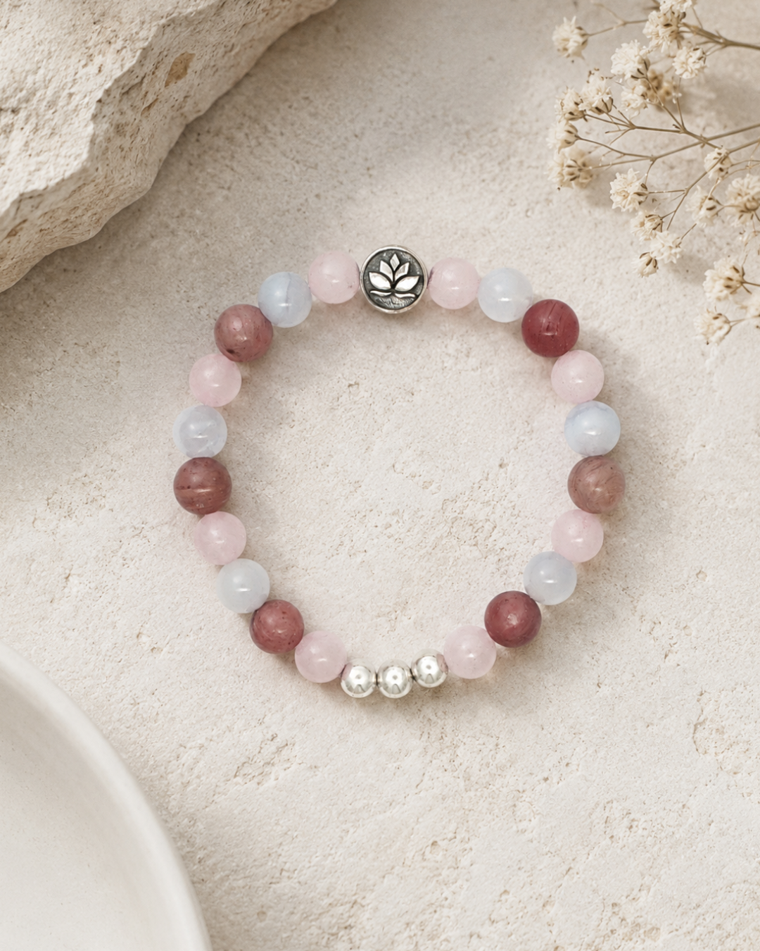Love Connection Lotus Bracelet styled on sandy stone surface with dried white flowers, showing rose quartz and rhodochrosite bead pattern