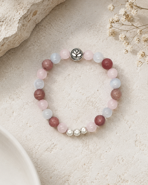 Love Connection Lotus Bracelet styled on sandy stone surface with dried white flowers, showing rose quartz and rhodochrosite bead pattern