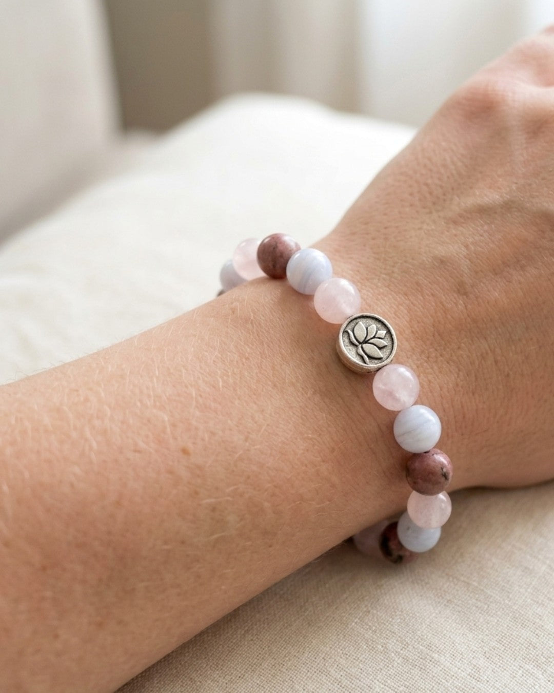 Love Connection Lotus Bracelet worn on a wrist, silver lotus charm at center, pink and mauve stone beads against cream fabric
