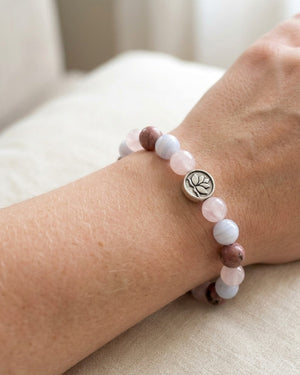Love Connection Lotus Bracelet worn on a wrist, silver lotus charm at center, pink and mauve stone beads against cream fabric