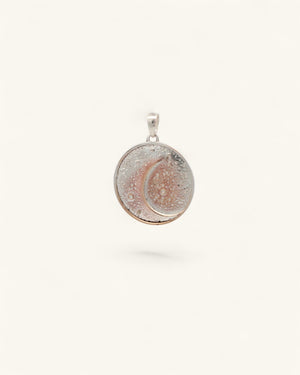Silver-plated crescent moon pendant at a three-quarter angle showing the textured disc face and silver bail loop