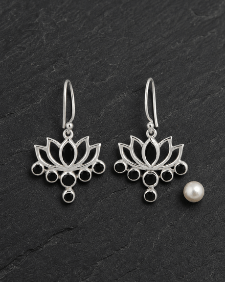 Sterling silver lotus flower drop earrings with black onyx stones on white marble surface