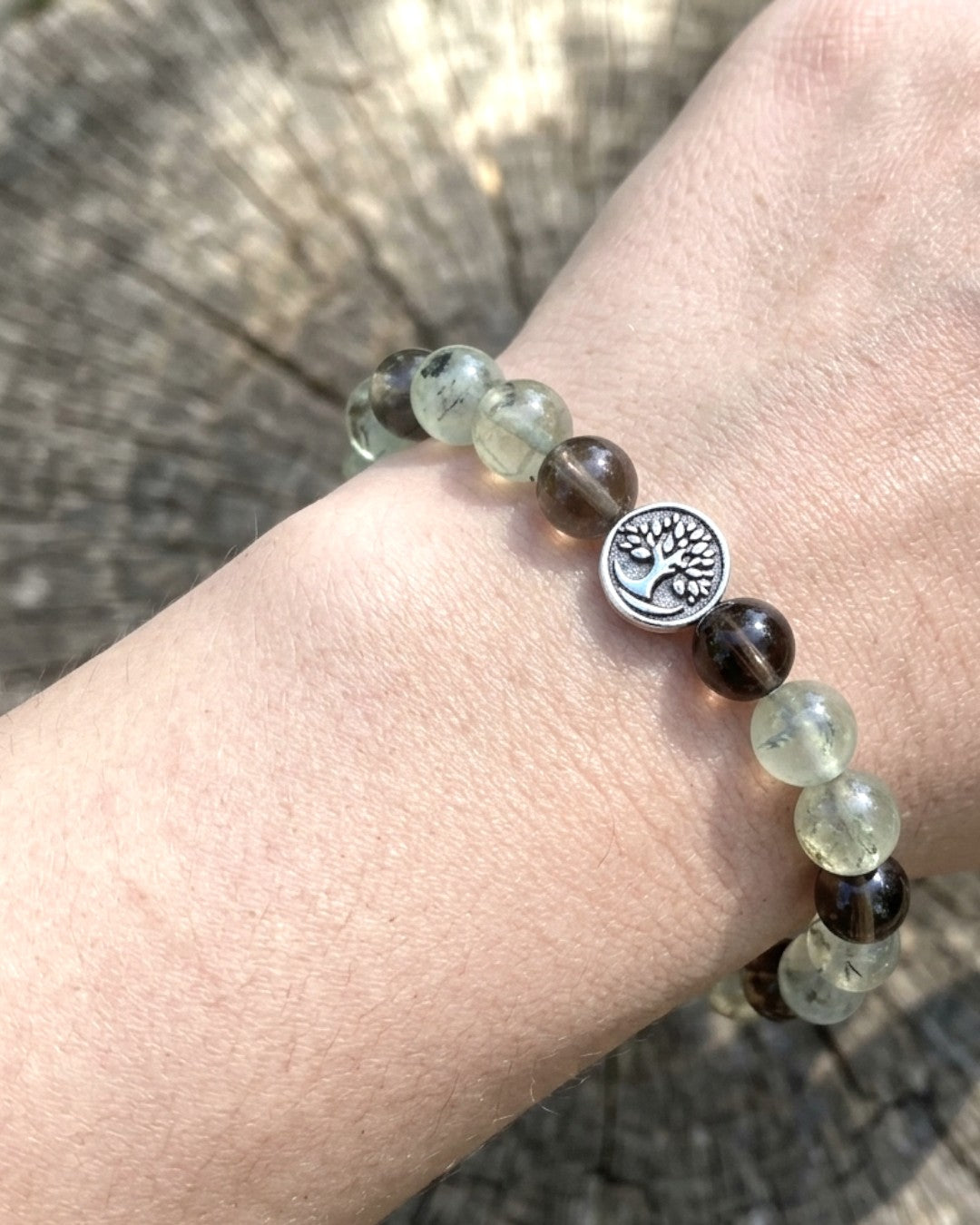 Tree of Life smoky quartz and prehnite bracelet worn on wrist with silver tree charm visible against wood background