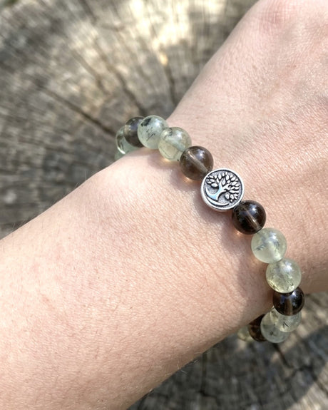 Tree of Life smoky quartz and prehnite bracelet worn on wrist with silver tree charm visible against wood background