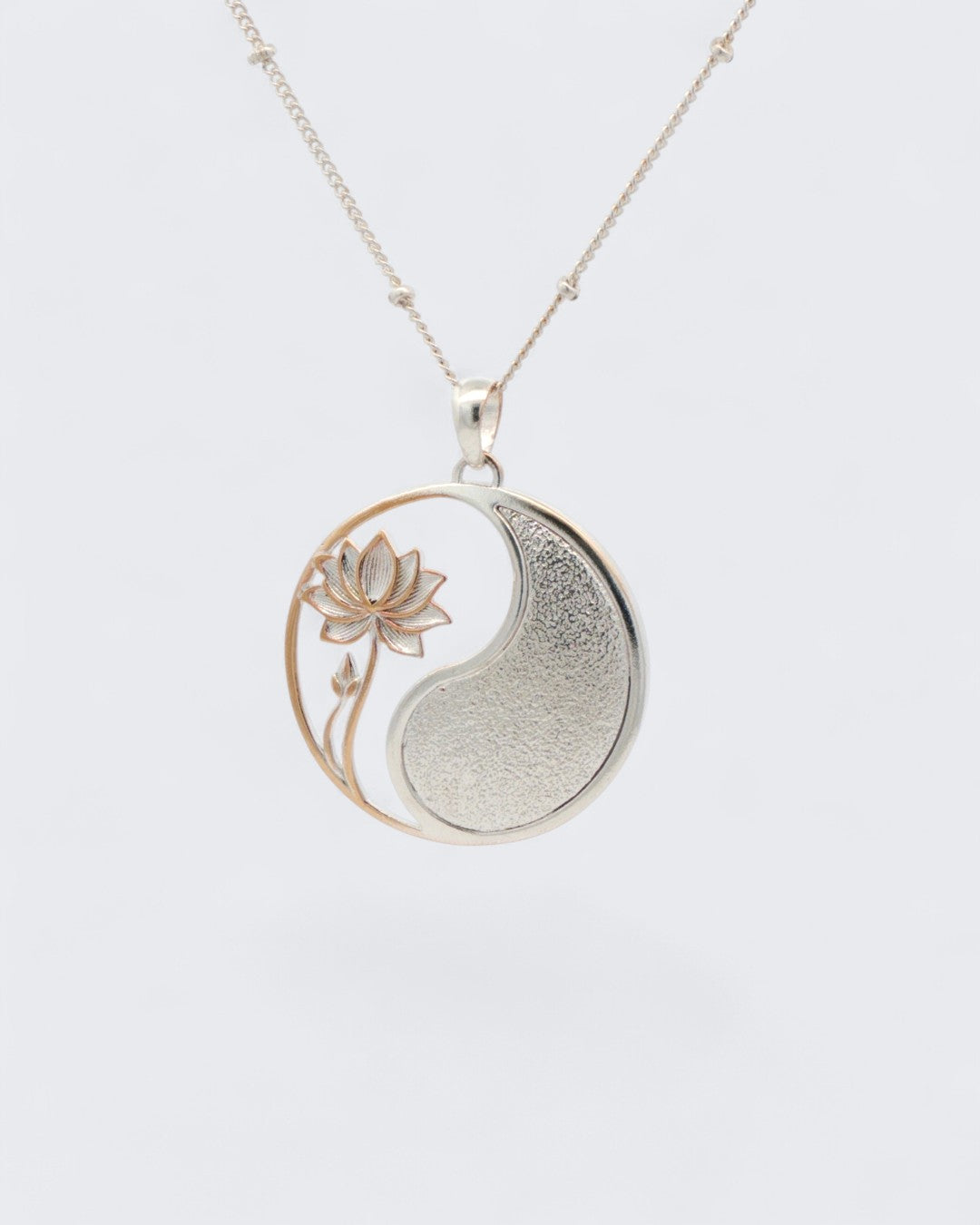 Yin yang lotus pendant hanging on a silver satellite ball chain, angled view showing rose gold lotus and silver yang half