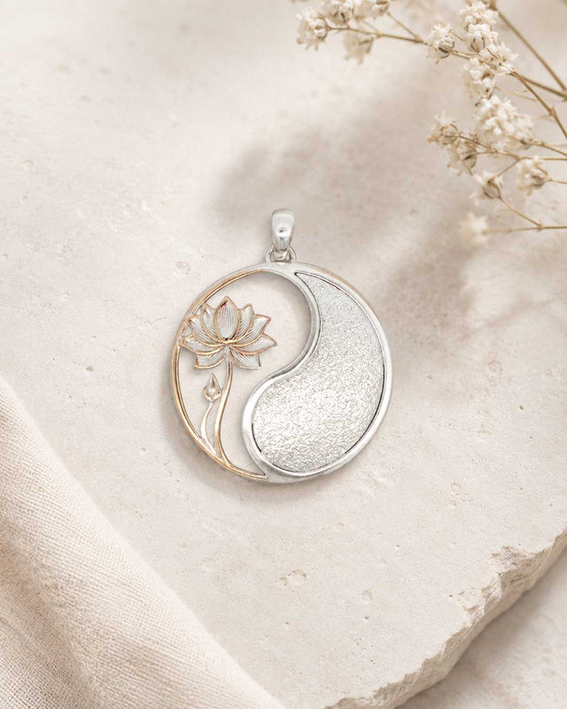 Yin yang lotus pendant resting on rough stone surface with linen fabric and dried baby's breath flowers in the background